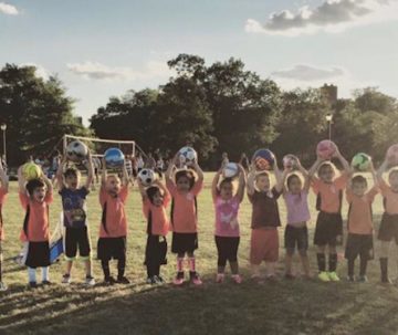 A group of children standing in the grass holding up frisbees.