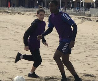 Two people playing soccer on the beach.